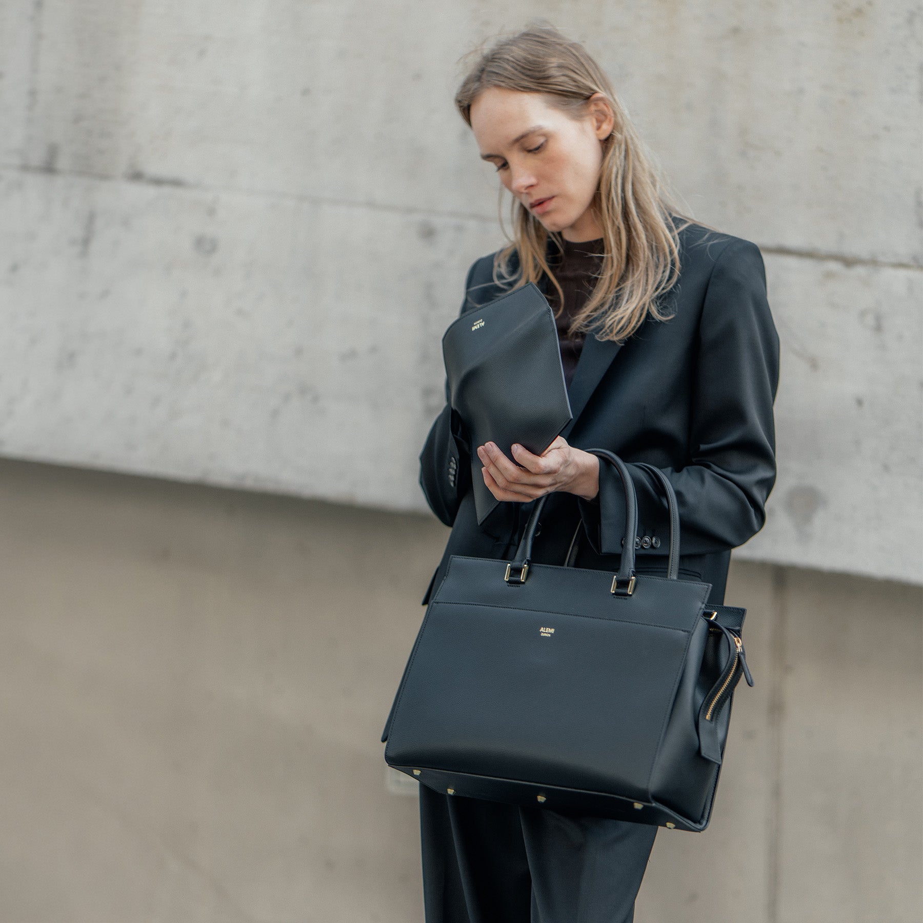 ALEMI Zurich | CENTRAL | Laptop Bag | Black | Pebbled Leather | Model holding bag and matching pouch