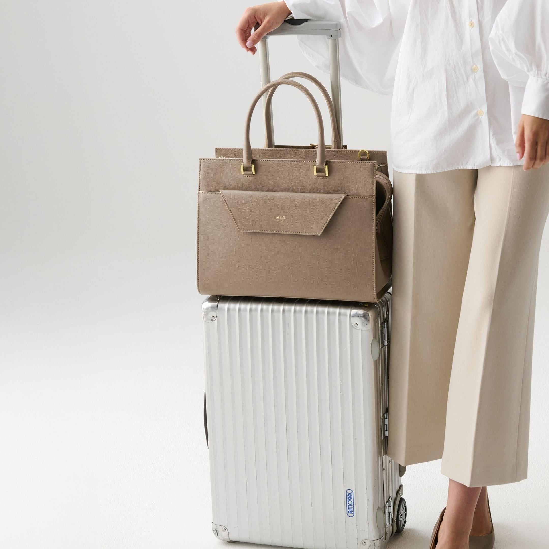 ALEMI Zurich | CENTRAL | Laptop Bag | Greige | Pebbled Leather | Model carrying bag on luggage