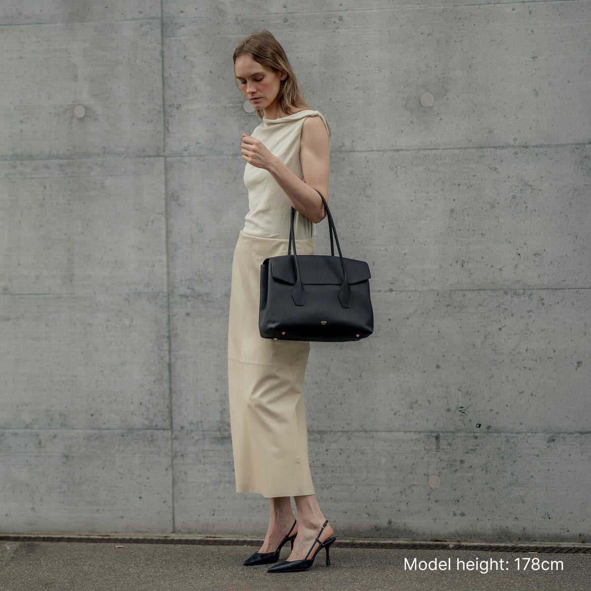 ALEMI Zurich | IDA | Laptop Bag | Black | Soft Grain Leather | Model carrying bag by top handle, full body