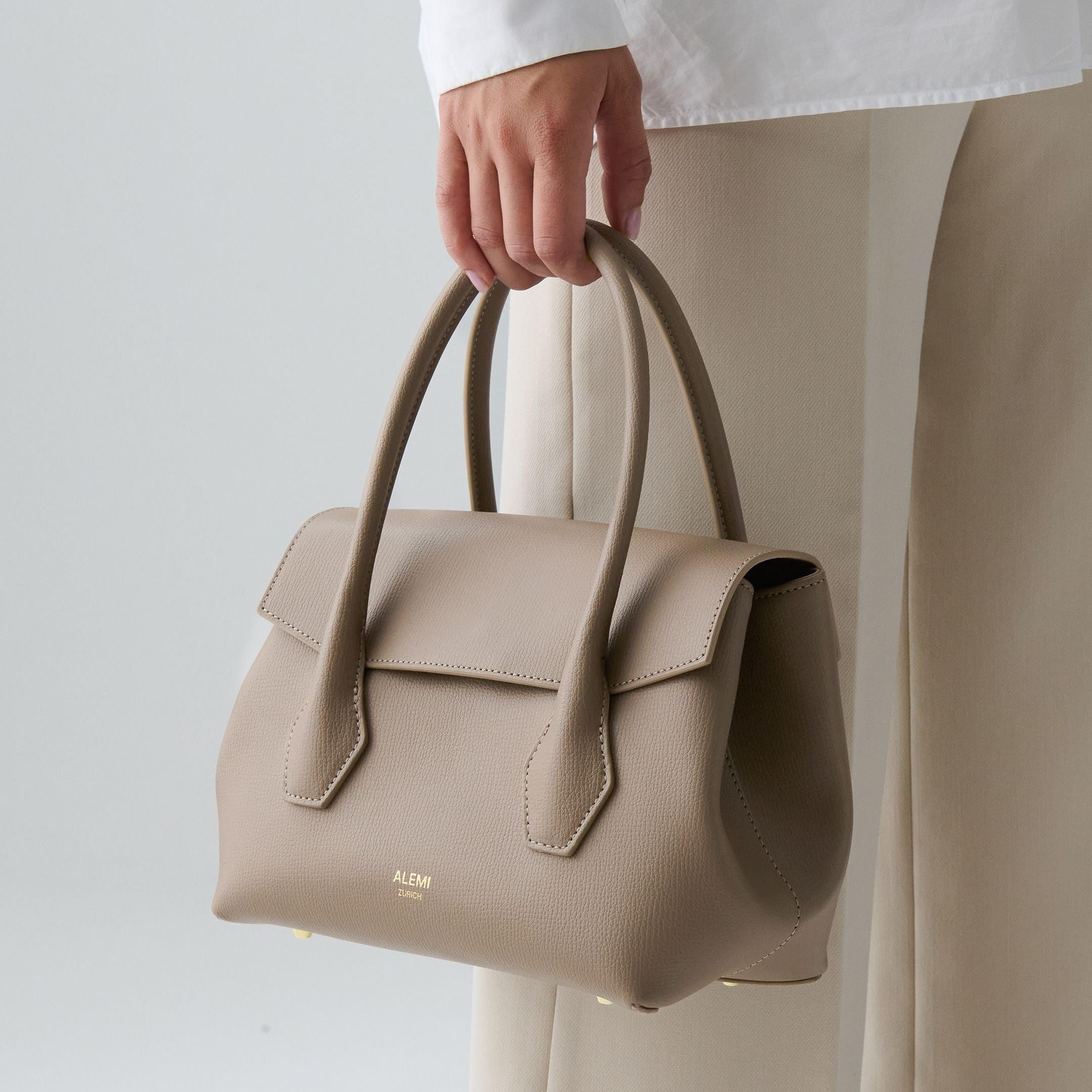 ALEMI Zurich | IDA SMALL | Small Bag | Greige | Pebbled Leather | Model carrying bag by handle