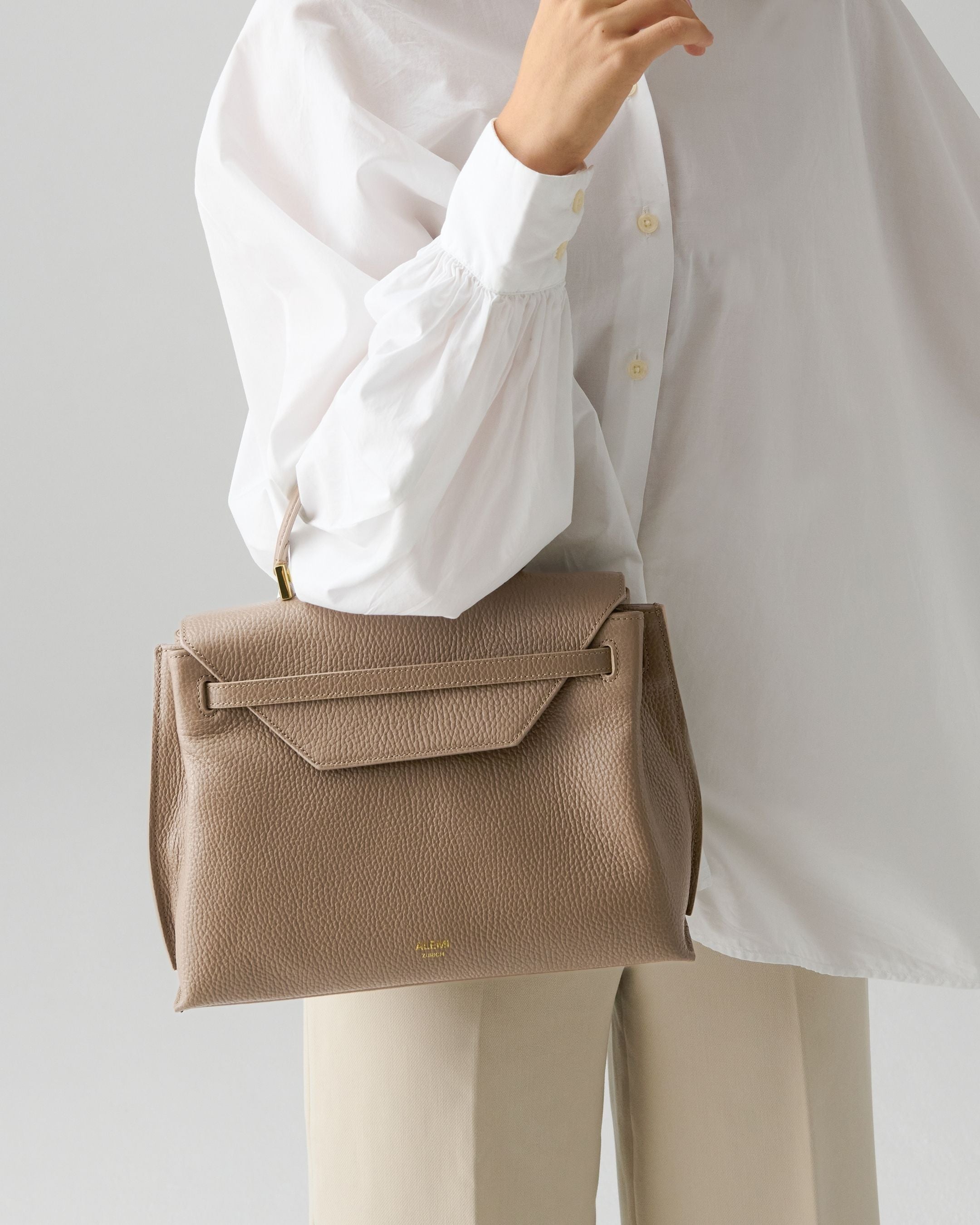 ALEMI Zurich | VIADUKT | Small Bag | Greige | Soft Grain Leather | Model carrying bag by handle
