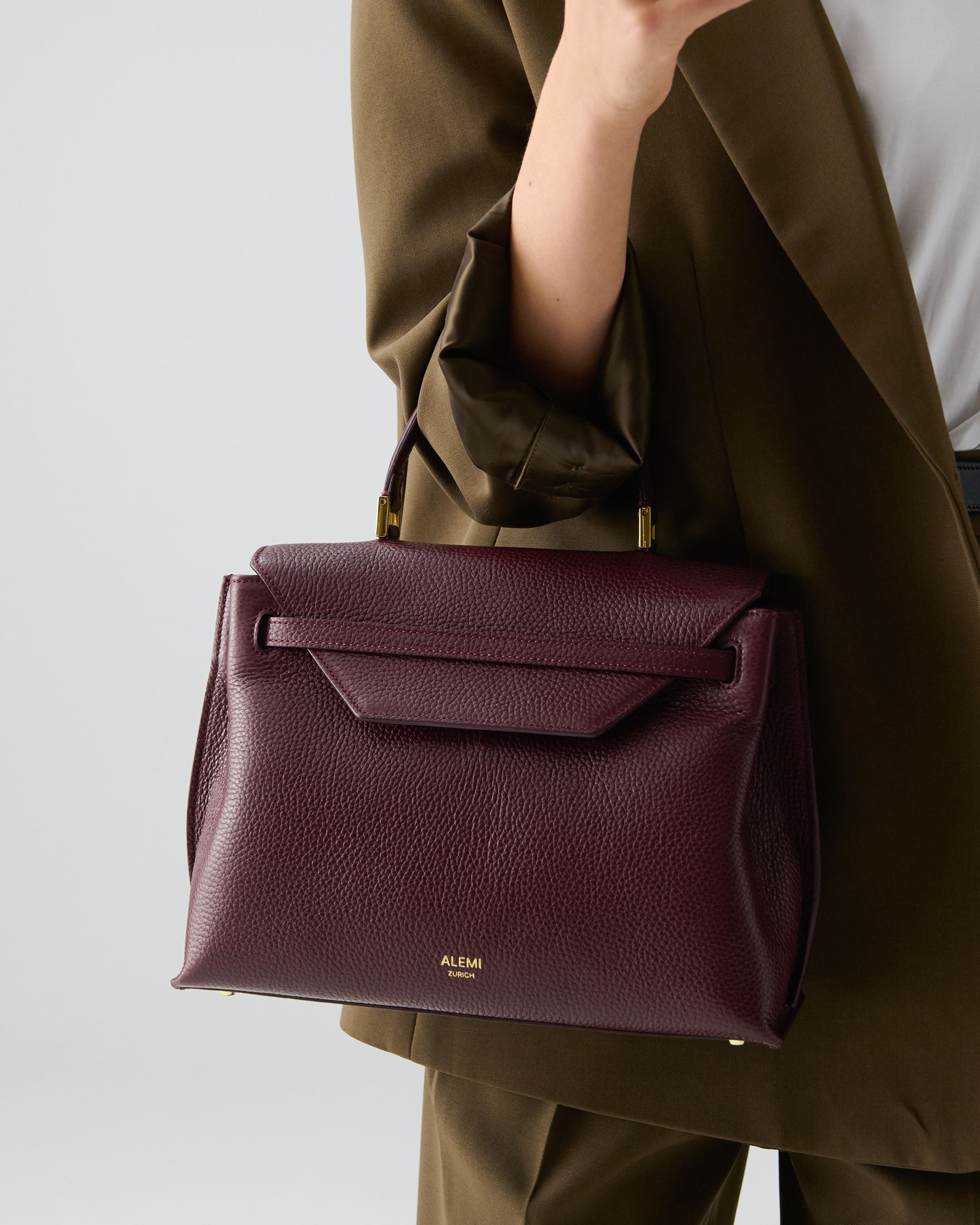 ALEMI Zurich | VIADUKT | Small Bag | Maroon Red | Soft Grain Leather | Model carrying bag by handle