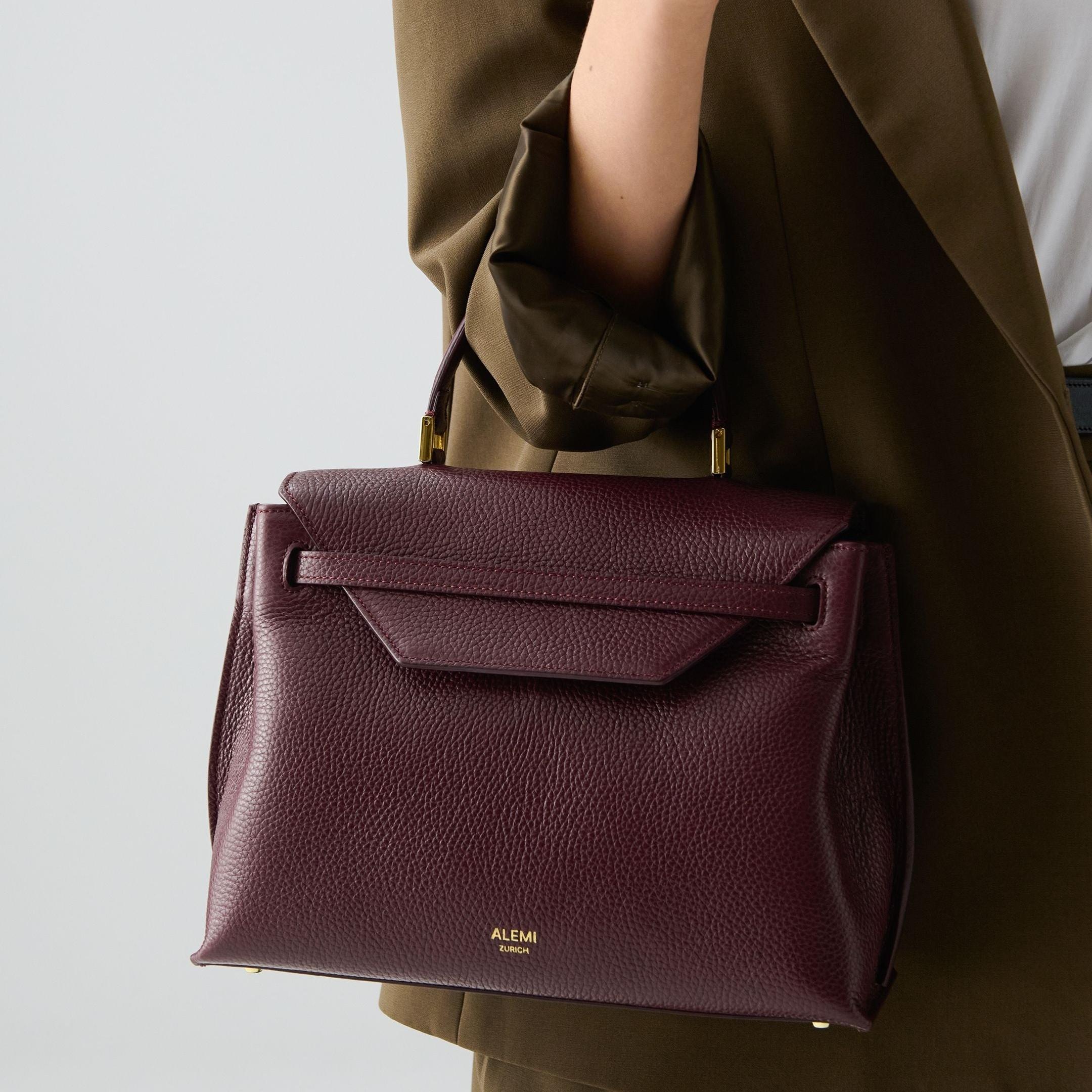 ALEMI Zurich | VIADUKT | Small Bag | Maroon Red | Soft Grain Leather | Model carrying bag by handle