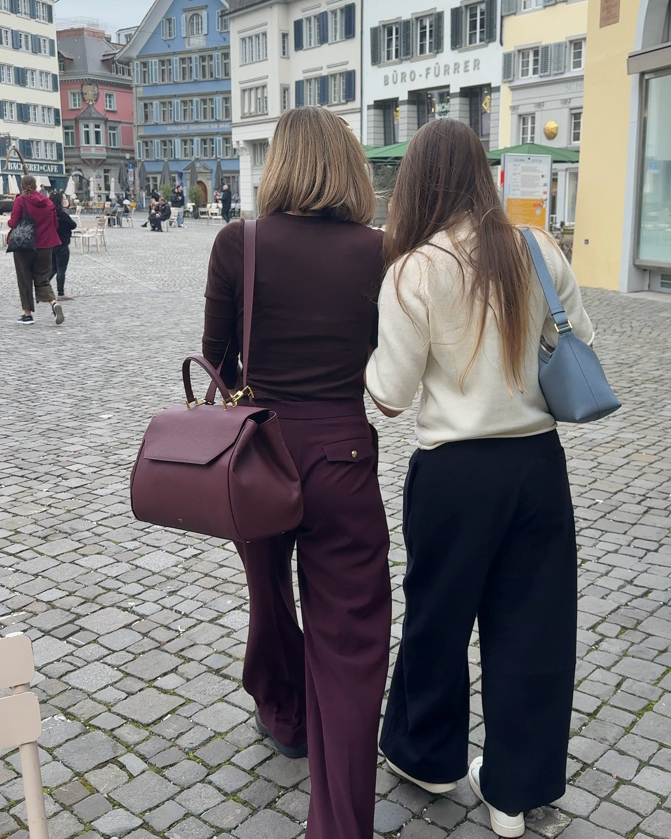 Two women walking on a cobblestone street in an urban setting wearing ALEMI BELLEVUE