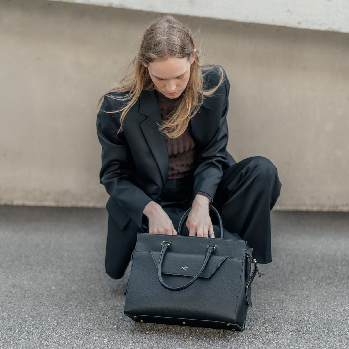 ALEMI Zurich | CENTRAL | Laptop Bag | Black | Pebbled Leather | Model crouching with bag