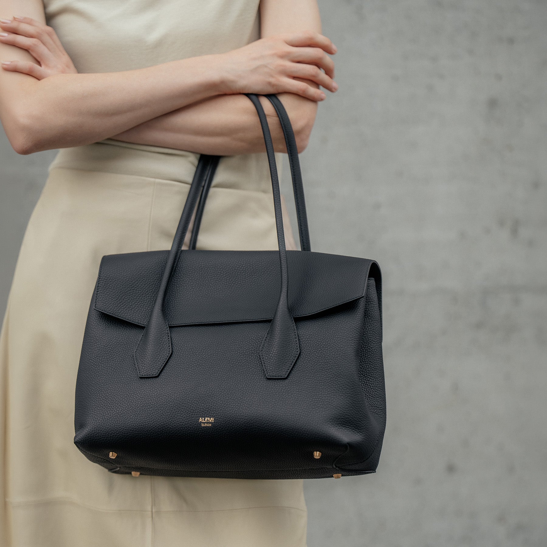 ALEMI Zurich | IDA | Laptop Bag | Black | Soft Grain Leather | Model carrying bag by top handle on arm