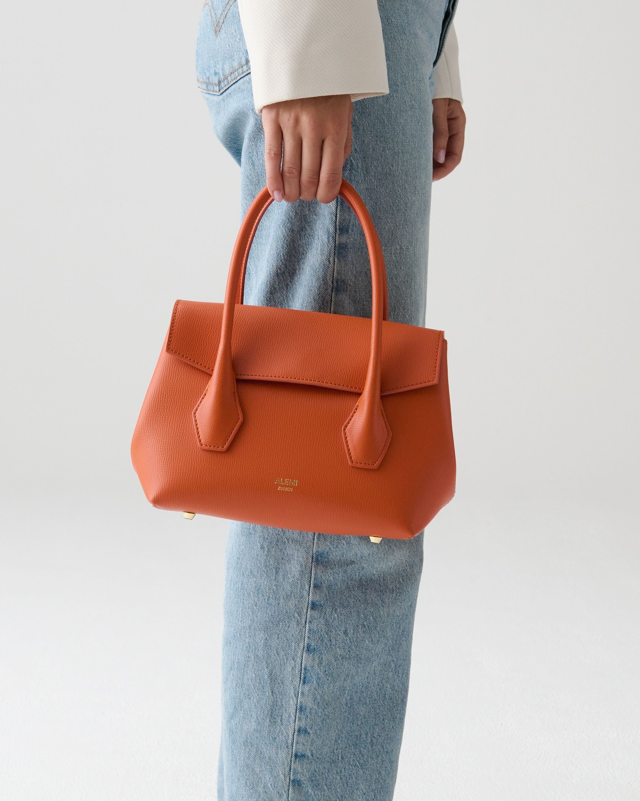 ALEMI Zurich | IDA SMALL | Small Bag | Deep Orange | Pebbled Leather | Model carrying bag by handle close up