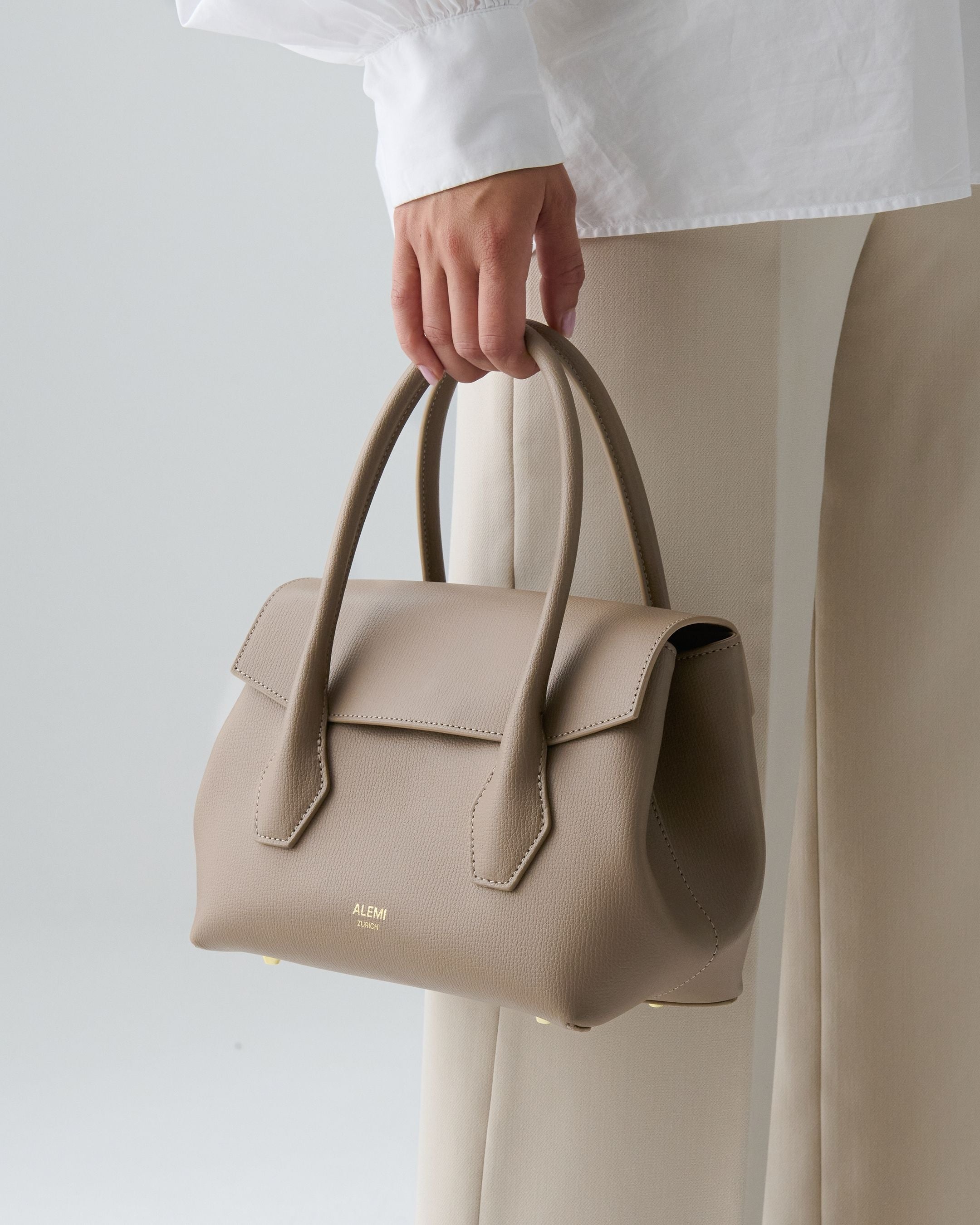 ALEMI Zurich | IDA SMALL | Small Bag | Greige | Pebbled Leather | Model carrying bag by handle