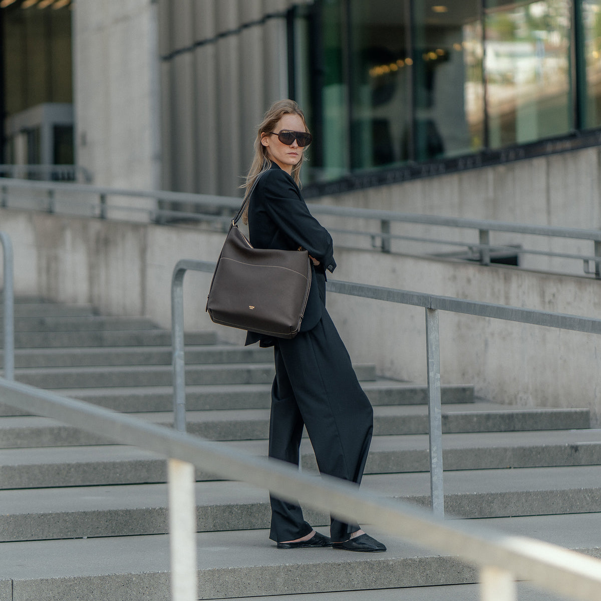 ALEMI Zurich | LETTEN | Laptop Bag | Dark Brown | Soft Grain Leather | Model carrying bag on shoulder on stairs
