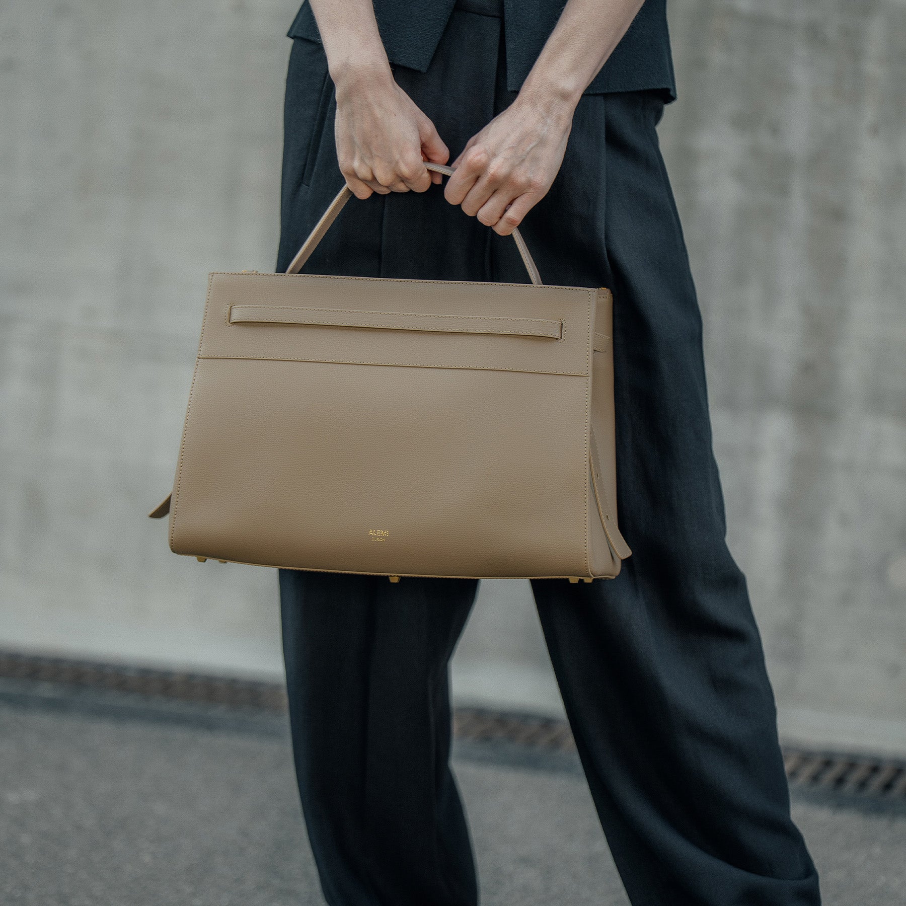 ALEMI Zurich | SEEFELD | Laptop Bag | Greige | Pebbled Leather | Model carrying bag by handle close up