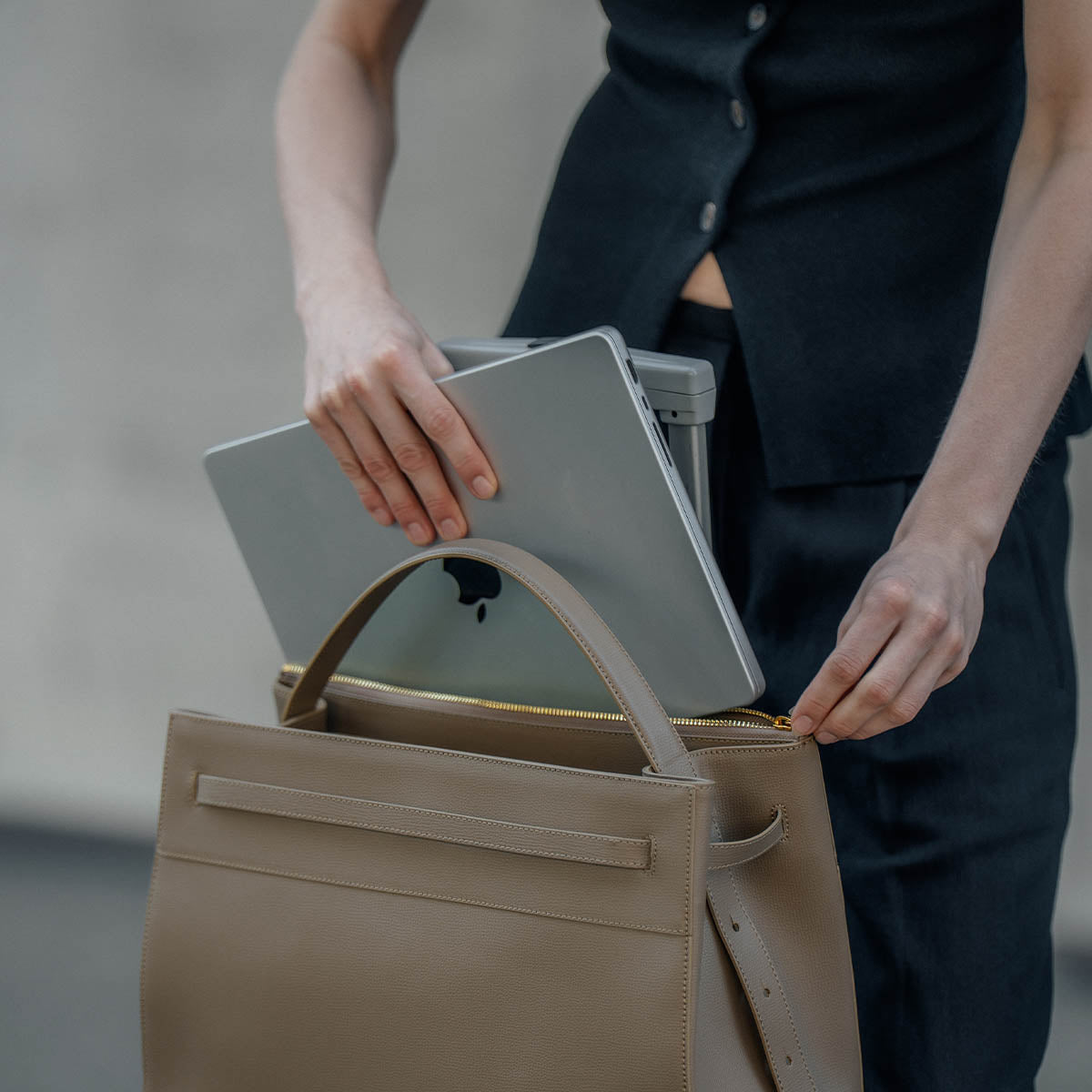 Laptop sliding into the separate laptop compartment of the ALEMI SEEFELD bag in greige Italian leather