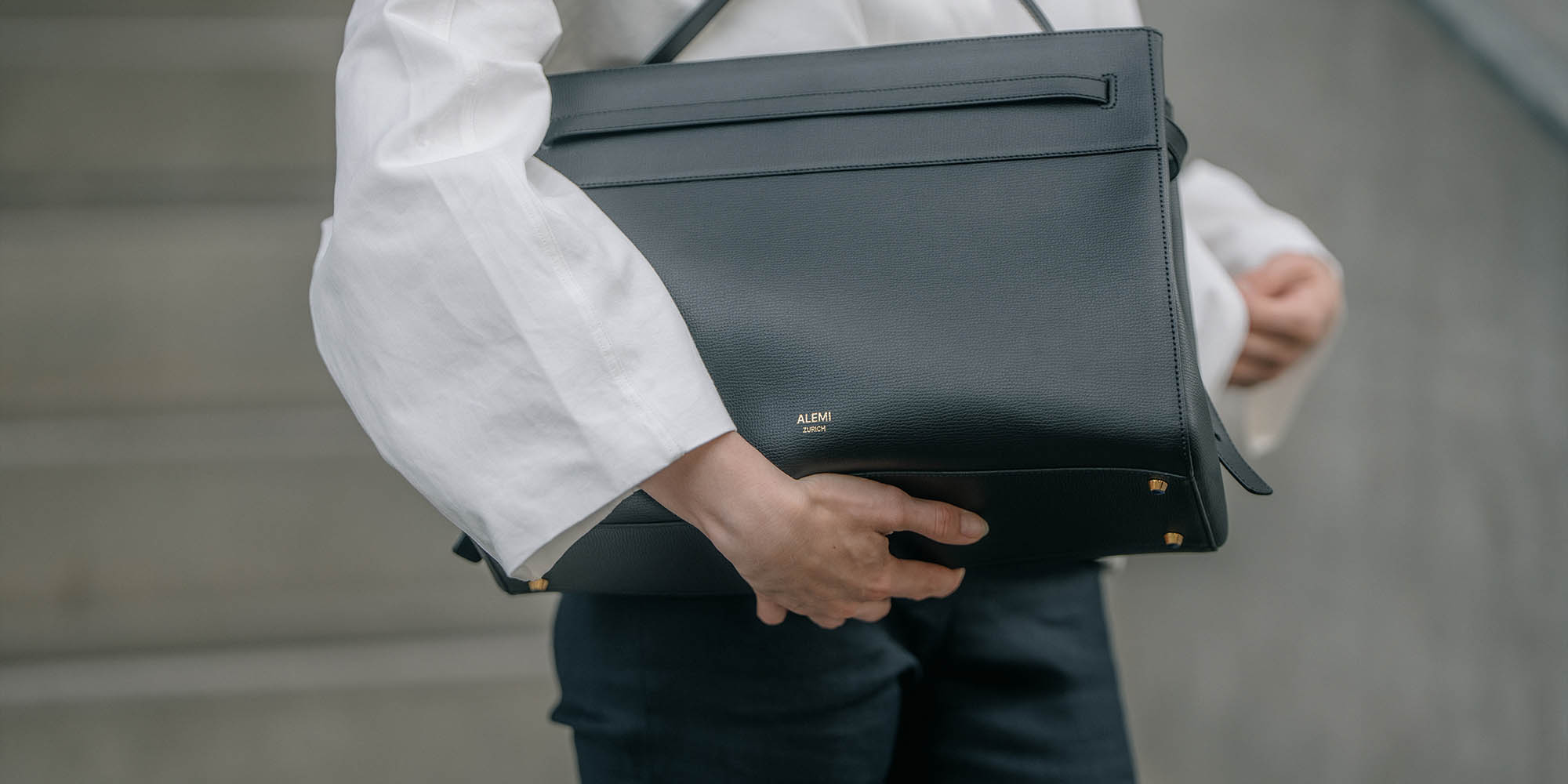 Woman in a white shirt carrying the ALEMI SEEFELD business bag in black pebbled Italian leather