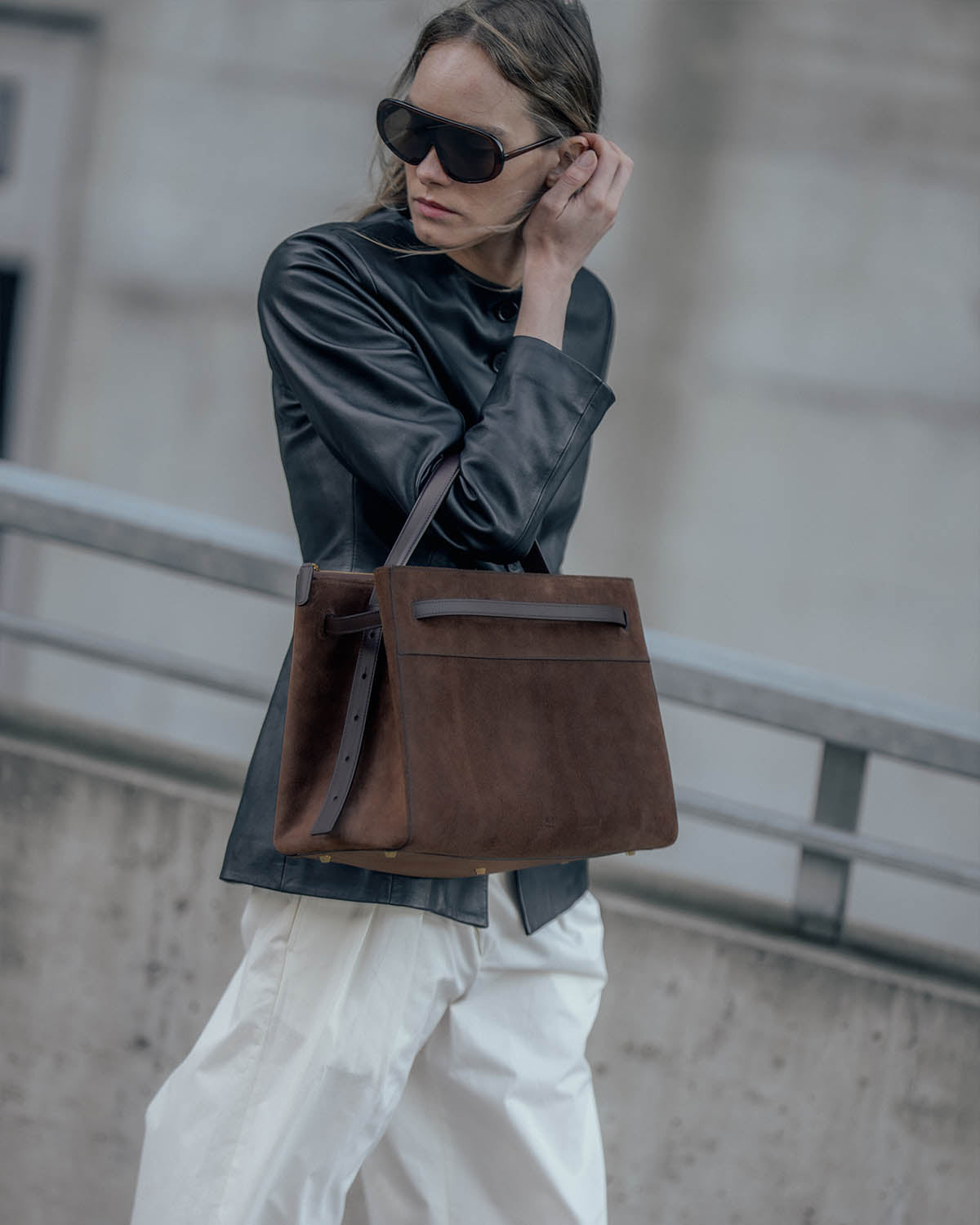 Woman in a leather jacket carrying the ALEMI SEEFELD bag in dark brown suede on her shoulder